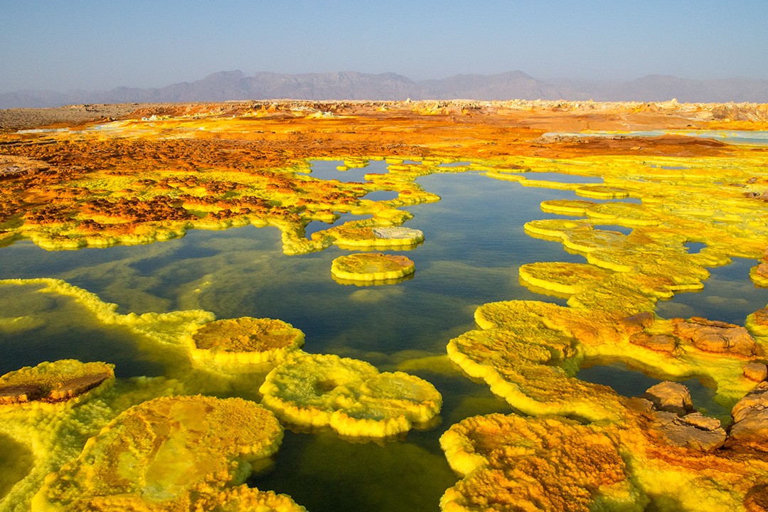 Expansive Dallol pools ringed by yellow sulfur formations.