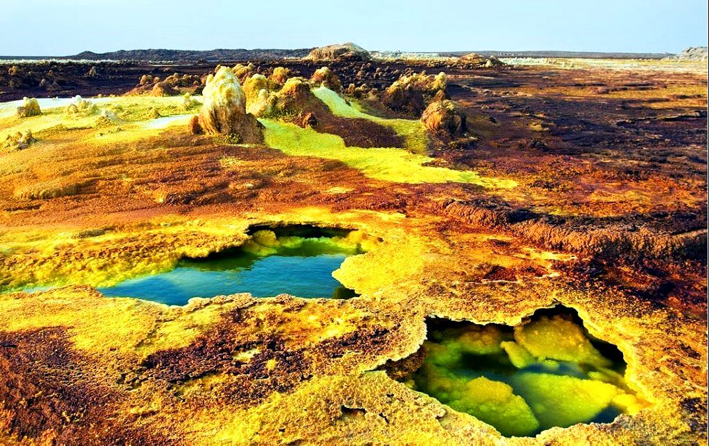 Vibrant acid pools and sulfur terraces at Dallol with striking green and yellow mineral bands.